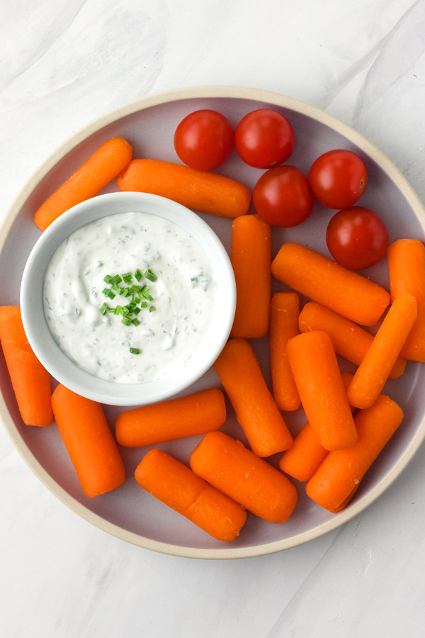 A blue plate with baby carrots, tomatoes, and a white bowl of dip.