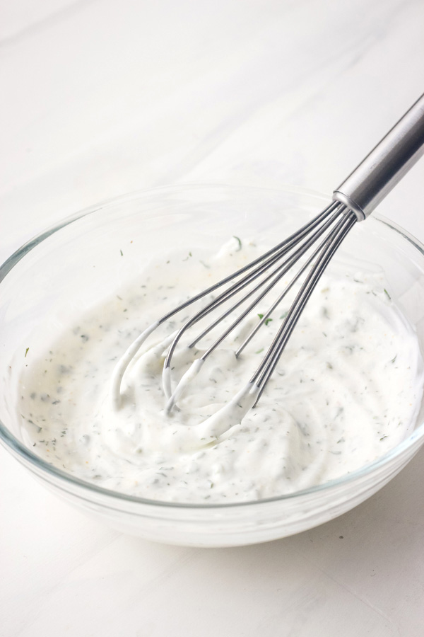 A small glass bowl with dip and a mini metal whisk.