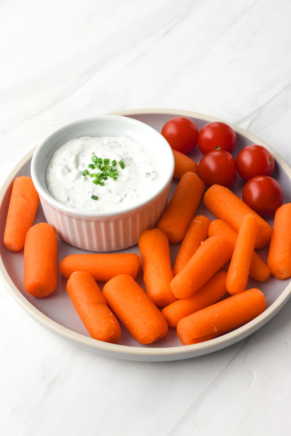 Carrots and cherry tomatoes on a blue plate with a small bowl of dip.