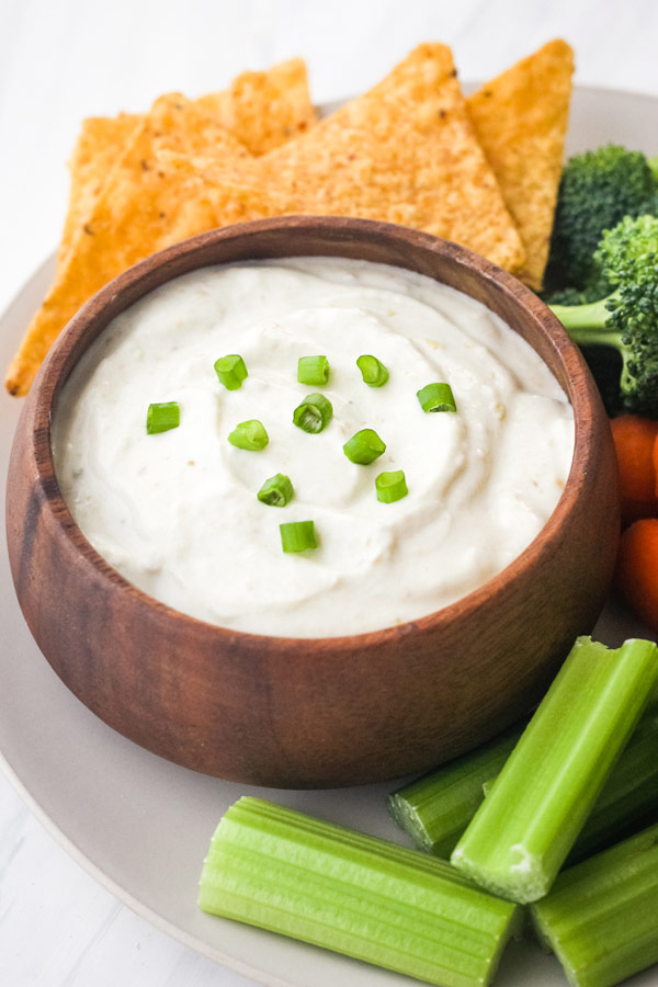 Small wooden bowl of dip with raw celery, carrots, broccoli, and chips.