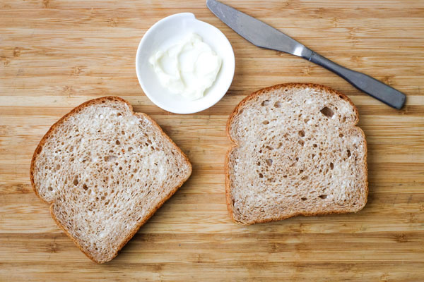 Bread slices spread with mayonnaise on a cutting board.