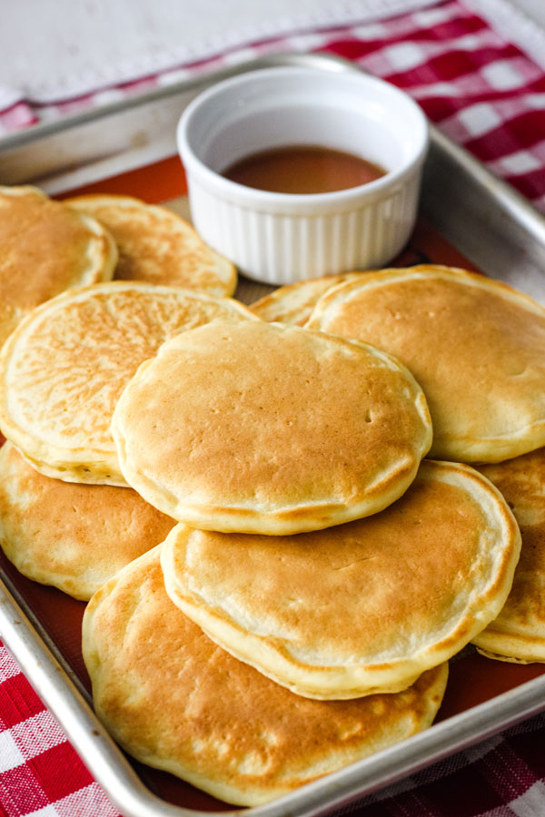 A metal baking pan full of pancakes on a red and white checked napkin.