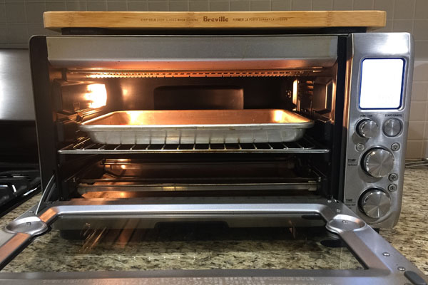 An open toaster oven with a baking pan on the middle rack.