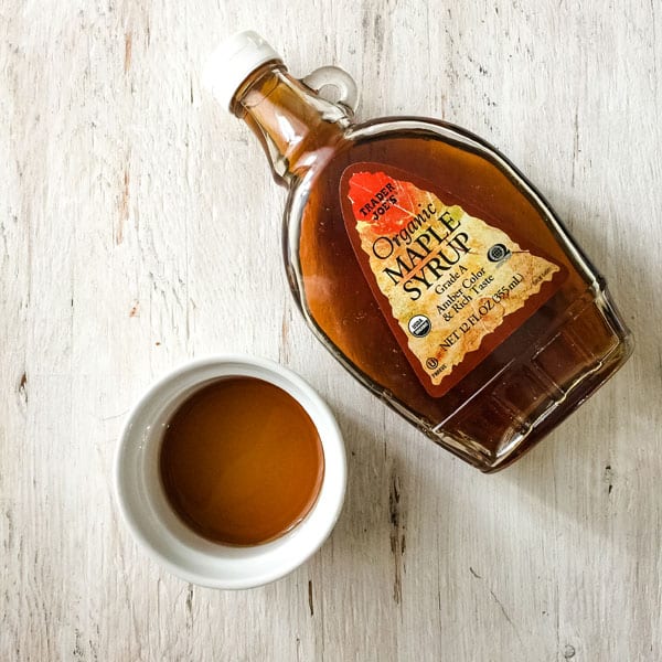 Bottle of maple syrup and a white ramekin filled with maple syrup.