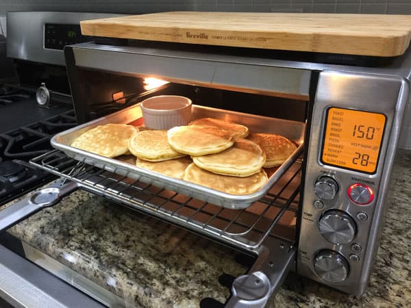 A pan with pancakes and a ramekin of maple syrup warming in a toaster oven.