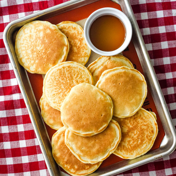 Overhead view of pancakes and a ramekin of syrup on a quarter sheet pan.