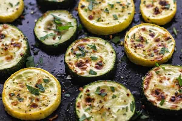 Broiled zucchini and summer squash on a black pan with fresh herbs.