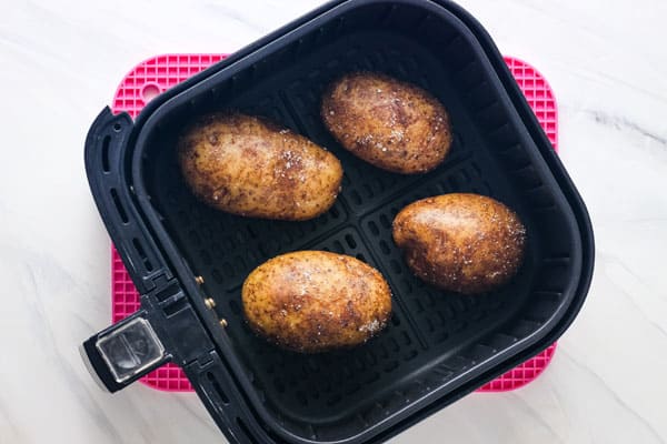 Overhead view of oiled potatoes in an air fryer basket.