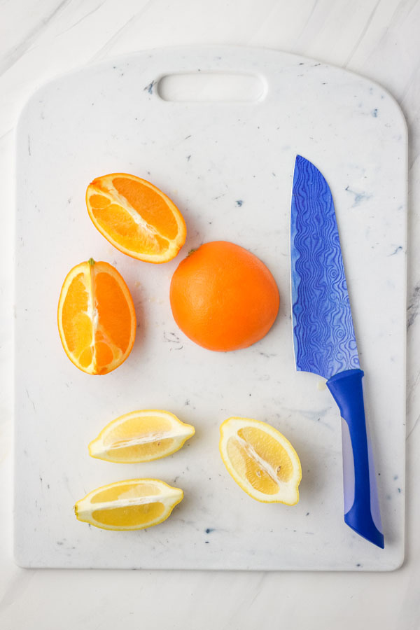 A cutting board with lemon and orange wedges with a blue knife.