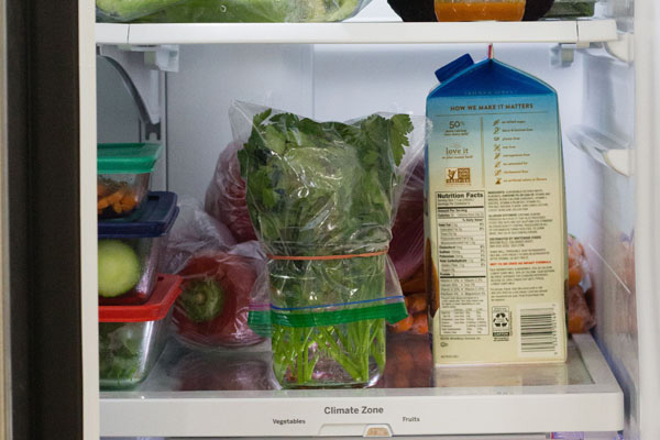 Herbs in a jar and carton of milk inside a fridge.