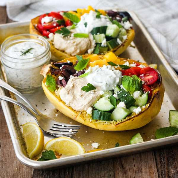 Two stuffed spaghetti squash with a jar of tzatziki sauce.