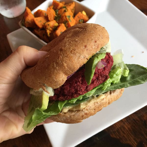 Hand holding a fat beet burger on a whole grain bun.