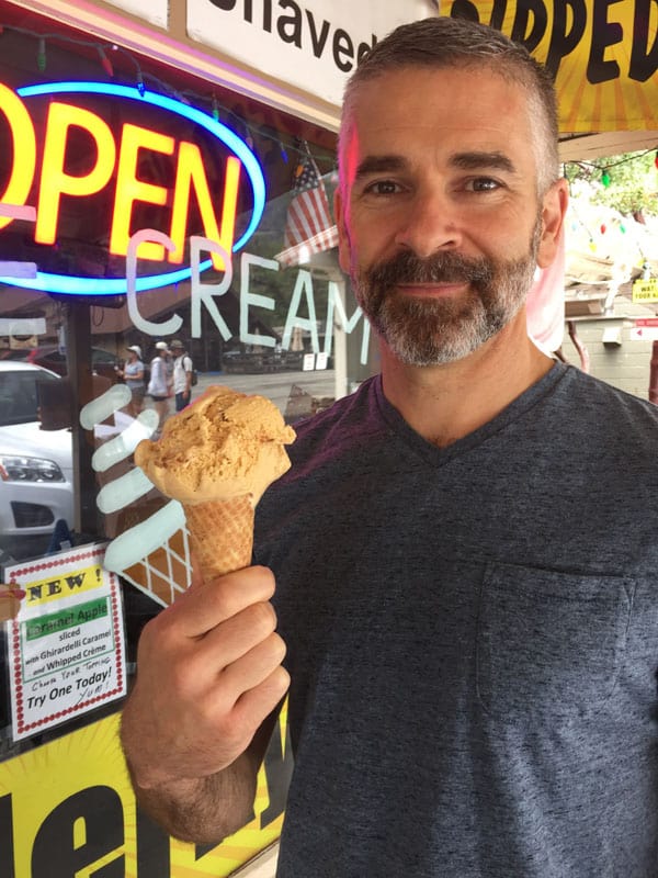 Man holding an ice cream cone with a large scoop of butter pecan ice cream.