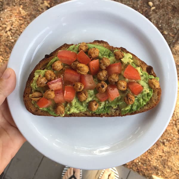 Avocado toast with tomatoes and roasted chickpeas on a white plate.
