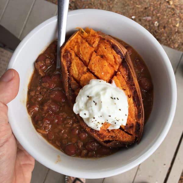 White bowl filled with vegetarian chili, baked sweet potato and Greek yogurt.