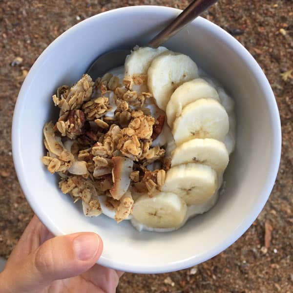 A white bowl with Greek yogurt, clumpy granola and sliced bananas.