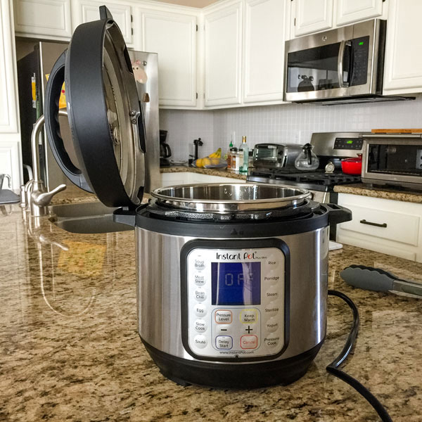 Instant pot on a counter with lid sitting on the side of the machine.