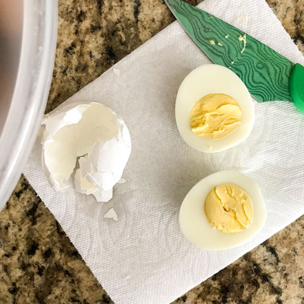 An egg sliced in half on a white napkin with a green knife.