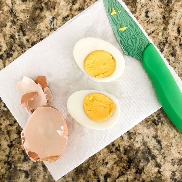 Egg sliced in half on a white napkin with a green knife.