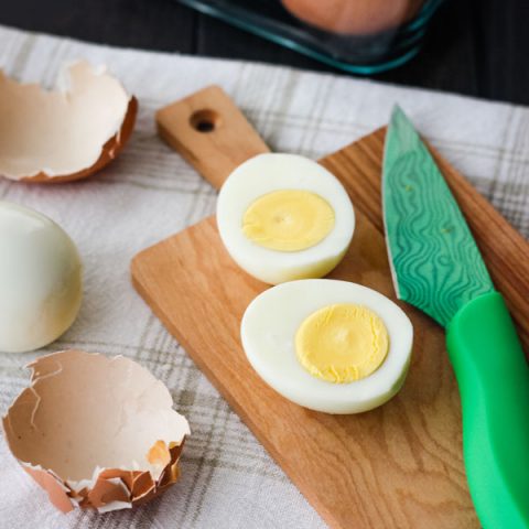 Hard cooked egg sliced open on a cutting board with a green knife.