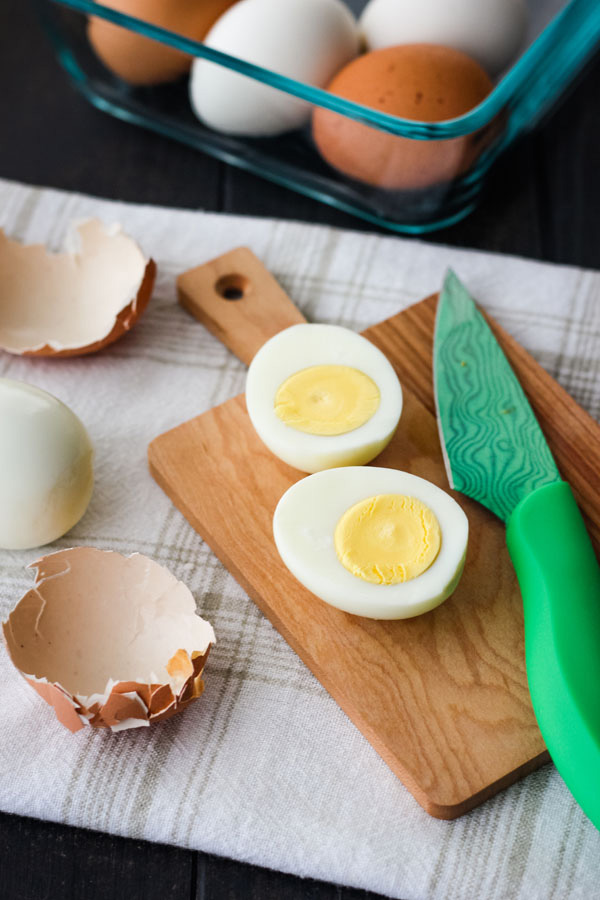 Hard cooked egg sliced open on a cutting board with a green knife.