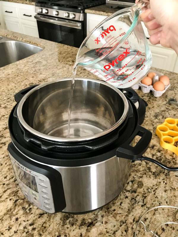 A hand pouring water from a glass measuring cup into an instant pot mini.