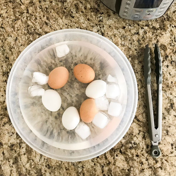 Hard boiled eggs in a large bowl filled with water and ice cubes.