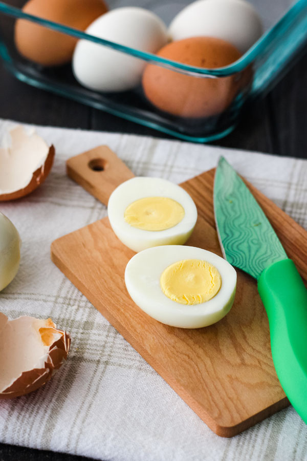 A hard boiled egg sliced in half on a mini cutting board with a green knife.