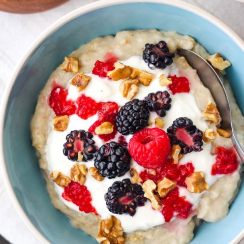 A blue bowl filled with oatmeal topped with yogurt, berries and nuts.