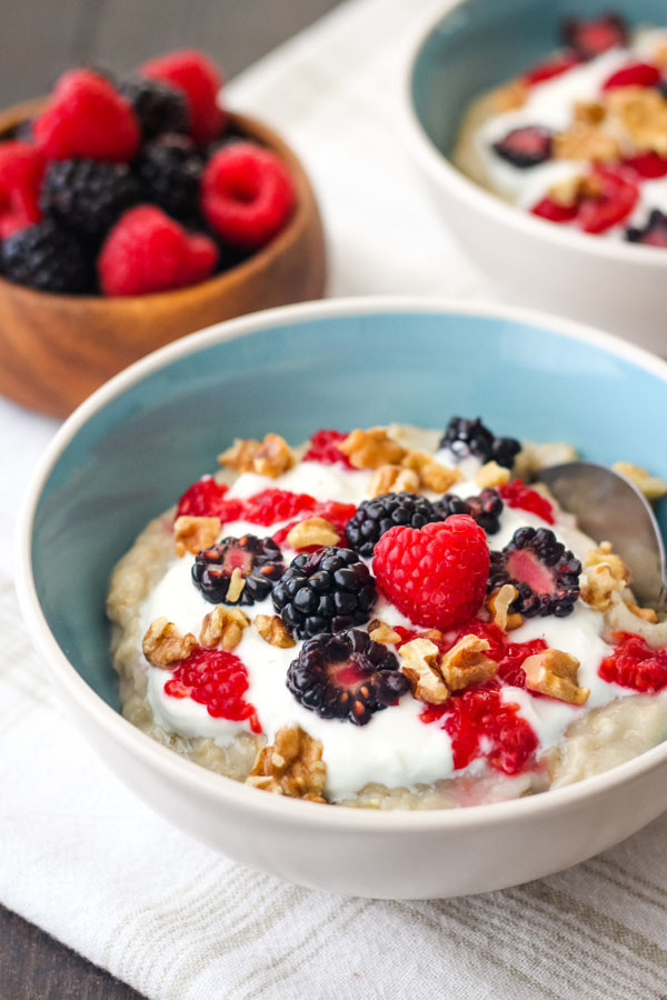 Two bowls of oatmeal on a table with fresh berries in a wooden bowl. 