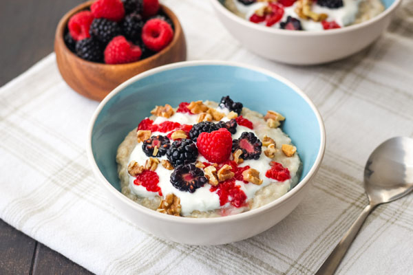 Oatmeal in a blue bowl with a small wooden bowl of berries.