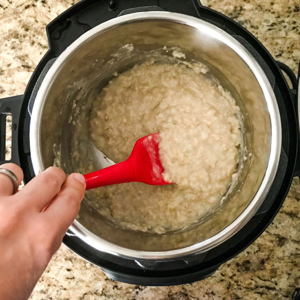 Oatmeal in a pot stirred with a red spoon.
