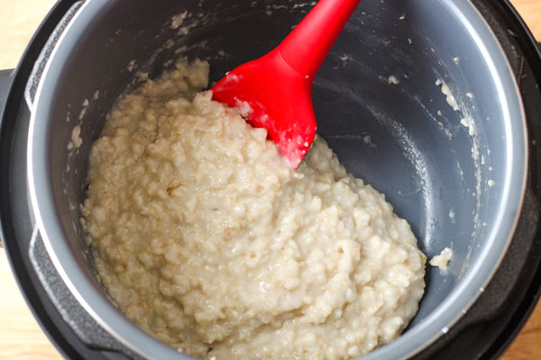 A red spatula stirring oatmeal inside a 3 quart instant pot.