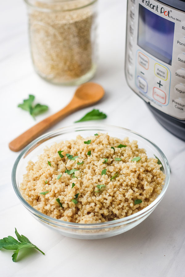 Cooked quinoa in a glass bowl next to a 3 quart Instant Pot.