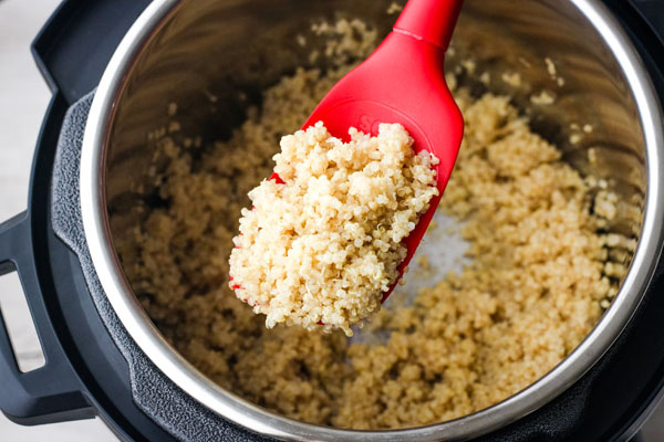 Fluffy cooked quinoa on a red silicone spoon.