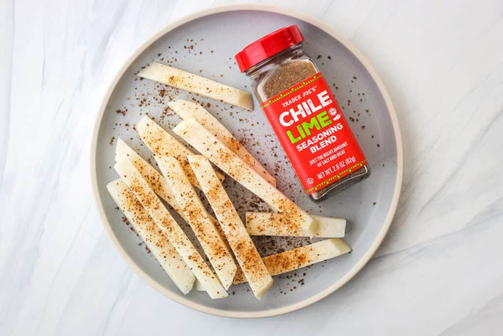 Seasoned jicama stick next to jar of chile lime seasoning.