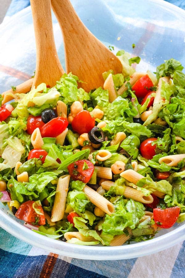 Large plastic bowl of salad with wooden spoons.