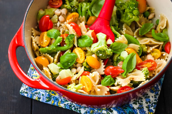 Small red dutch oven full of cooked vegetables and pasta.