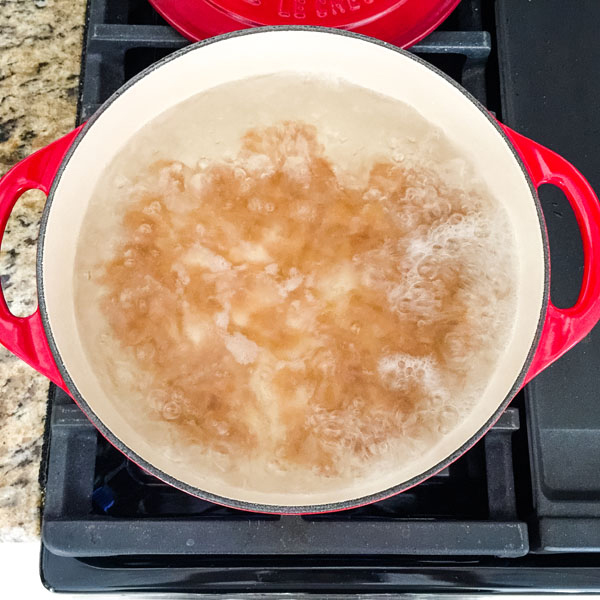 Red dutch oven full of boiling water and pasta on a stovetop.