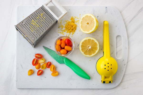 Cutting board with sliced grape tomatoes and lemon with grater and juicer.