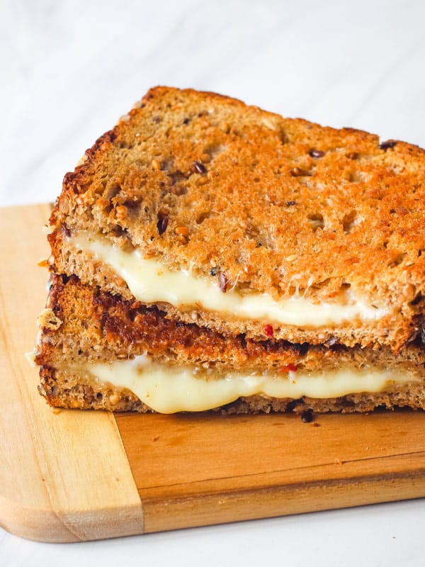 Melty grilled cheese slices stacked on a cutting board.