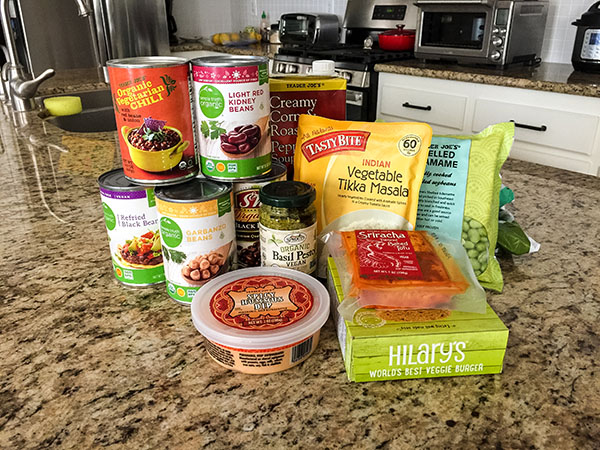 Can of beans, hummus, veggie burgers, soup and frozen vegetables on a kitchen counter.