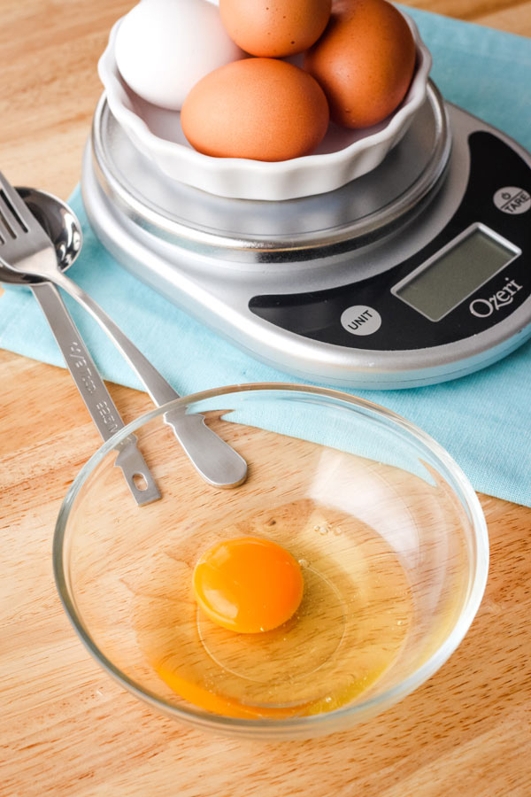 An egg in a bowl in front a scale, measuring spoon, and fork.