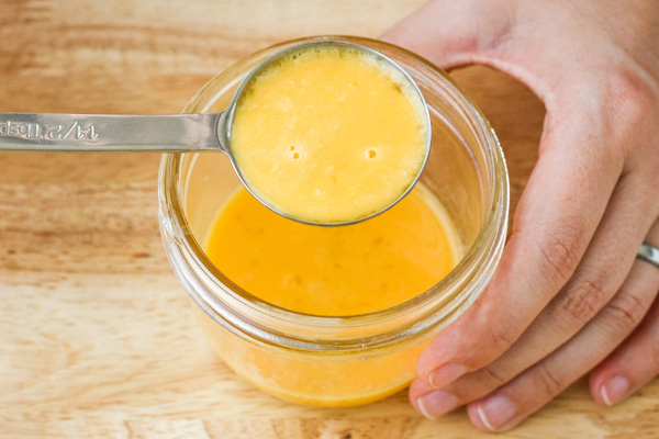 Hand holding measuring spoon filled with beaten egg.