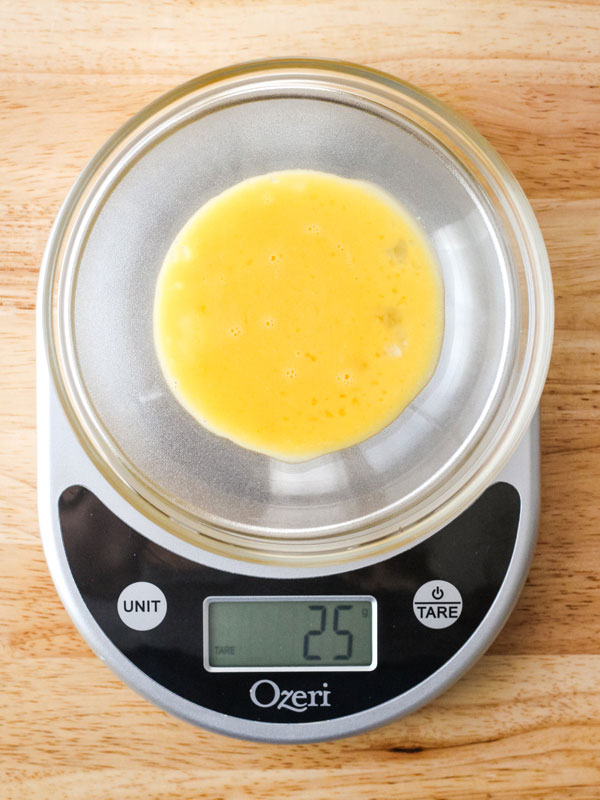 Beaten egg in a bowl on a digital scale with 25 grams displayed on the screen.