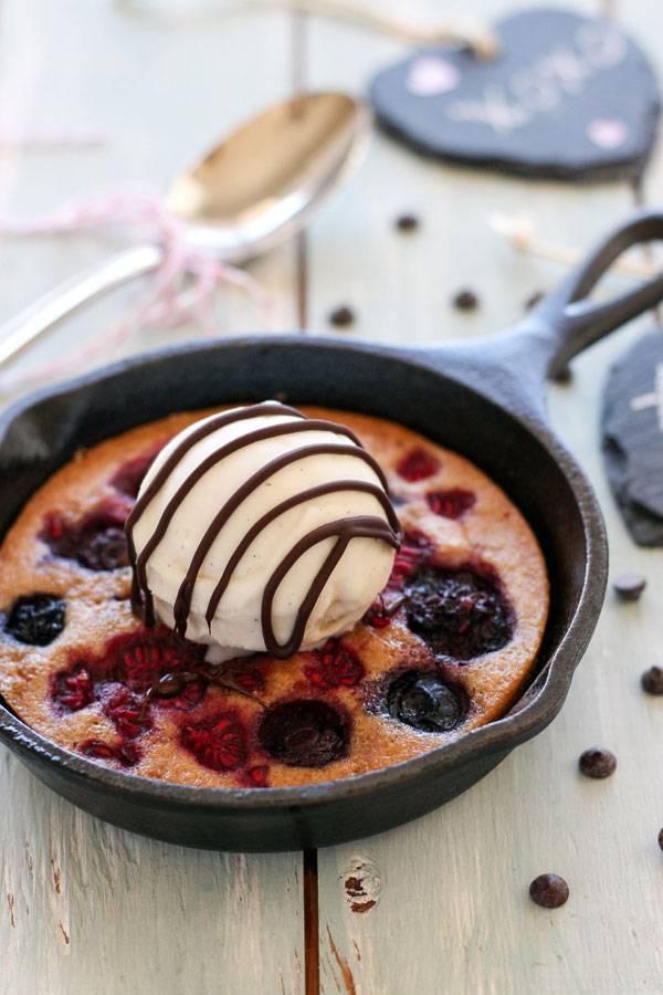 A mini skillet cake topped with vanilla ice cream next to a spoon.