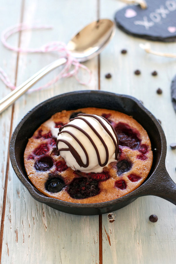 Chocolate chips scattered around a mini skillet on a blue wooden table.