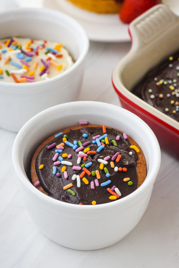 Ramekins of cake frosted and topped with rainbow colored sprinkles.