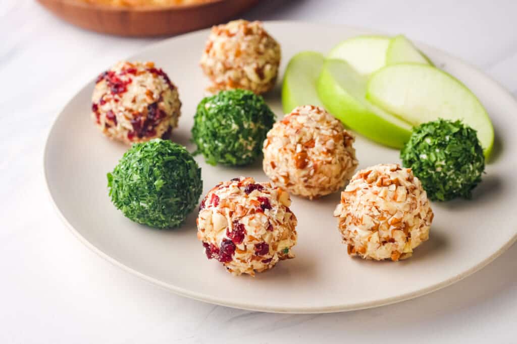 Variety of mini cheese balls on a plate with apple slices.