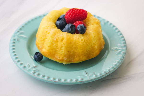 A small blue plate with a mini lemon bundt cake topped with fresh blueberries and raspberries.